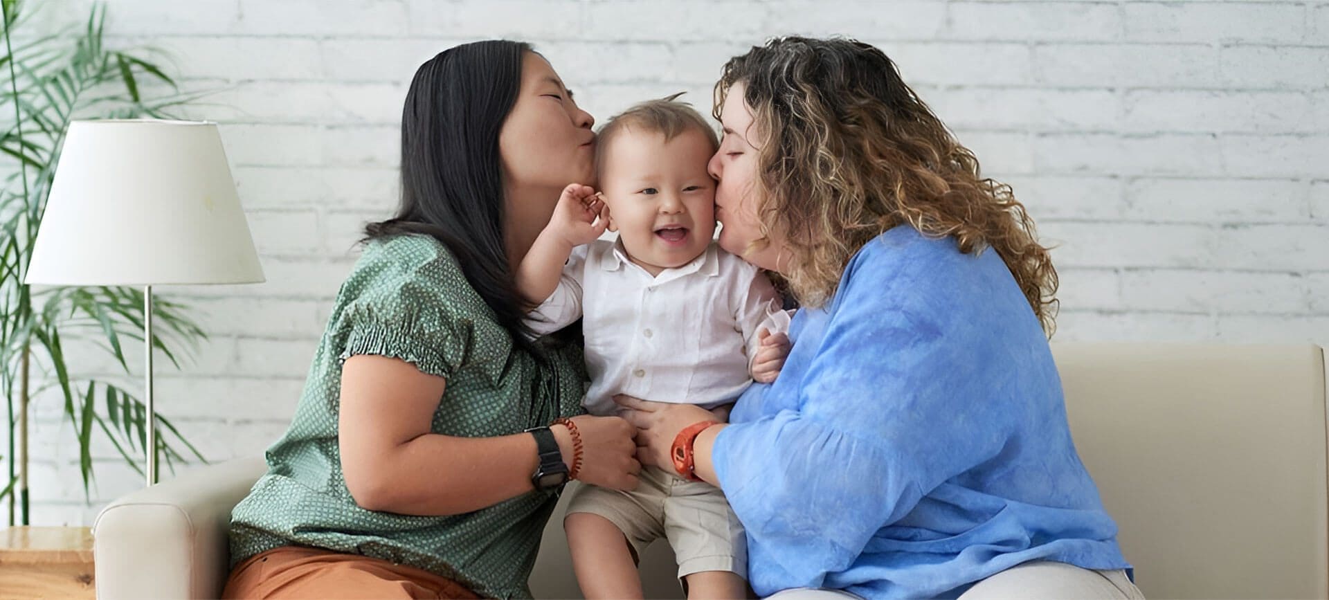 Two women kissing a baby boy on the cheek.